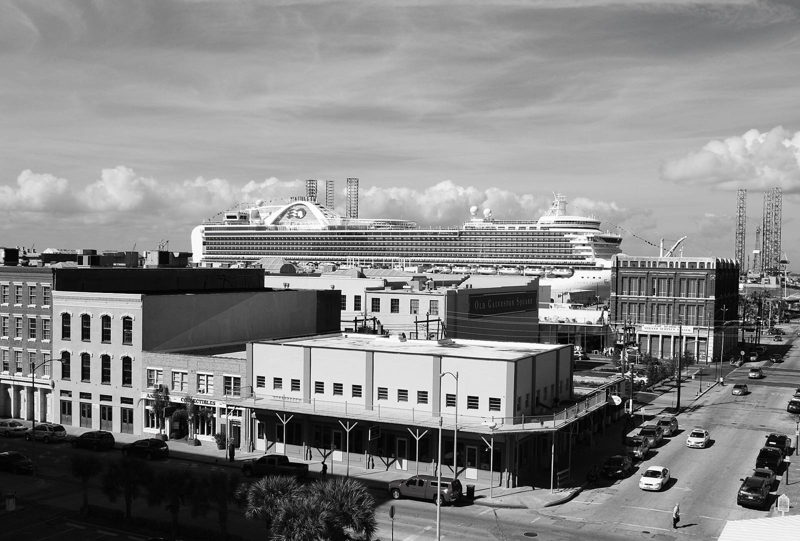 A cruise ship docked behind the Strand's brick buildings, in black and white